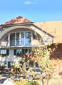 Two-story house with a large arched balcony, green shutters, and a well-maintained garden.
