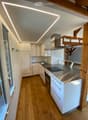 Modern kitchen with white cabinets, stainless steel appliances, wooden flooring, and built-in LED lighting.
