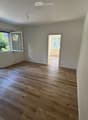 Empty room with light wooden flooring, white walls, and large windows with open sliding doors leading to an outdoor area.