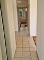A long, narrow hallway with tiled flooring and white walls, leading to a room with a small table and chair visible at the end.