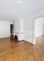 Empty room with wooden parquet flooring, white walls, and large windows. Features a fireplace with a decorative screen and a radiator under the windows.