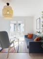 modern living room, open plan, glass doors, bright, wooden floor, colorful rug, grey couch, wooden chair, lamp, bamboo plant, TV