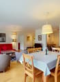 modern dining area, wooden dining table, wooden chairs, red sofa, floor lamp, window, picture frames, cabinet, tableware, flowers