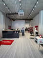 Interior of an office with a grey and white color scheme, carpeted floor, multiple modern fixtures, reception desks, chairs, tables, and decorative items