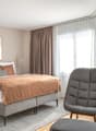 bedroom with bed, bedside tables, picture frame, curtains, chair, ottoman, carpet