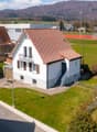 Detached house, brown roof, white walls, balcony, garage, garden, tennis court in the background