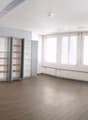 Large open room with white walls, hardwood flooring, and multiple built-in shelving units along the walls. The room has several large windows providing natural light.
