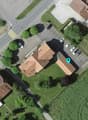 A two story house with brown roof, parking area with several cars parked, trees in the area