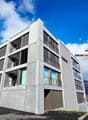 Modern apartment building, concrete exterior, multiple floors, balconies, windows, entrance