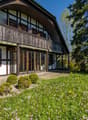 Traditional house, wooden exterior, white walls, wooden balcony, glass doors, large windows, surrounded by greenery