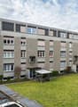 4 story apartment building, grey exterior, multiple windows, bicycles parked outside, green lawn in front