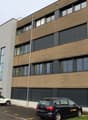 3 story modern office building, brown exterior, windows, parking area
