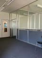 Empty office room with glass partitions, gray carpet, black chairs, a door, and potted plants