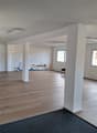 empty room, hardwood floor, white walls, 2 white pillars, 3 windows, radiator, ceiling lights