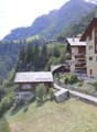multiple wooden buildings, located on the slopes of a mountain, surrounded by greenery, offering a stunning panoramic view of the surrounding mountains