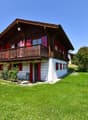 2-story wooden chalet, red shutters, balcony, white walls, sloping roof, garden
