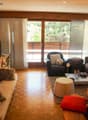 Spacious living room with large windows overlooking a balcony, hardwood floors, comfortable sofas and armchairs, coffee table, and various decorative elements.