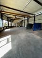 Large open space with concrete floor, exposed ceiling beams, and windows along the walls. The space appears to be a warehouse or industrial facility with some equipment and storage items visible.