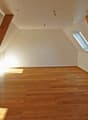 Spacious attic room with wooden beams, hardwood flooring, and a skylight window providing natural light.