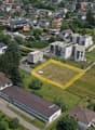 Aerial view of a residential area with multi-story apartment buildings, houses, and a large open green space with a parking lot visible.