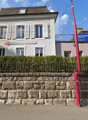 White house, red roof, white shutters, stone wall, greenery, parking pole