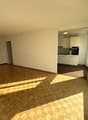 Wooden flooring, sun-drenched, large windows, empty room, white kitchen with black oven, white cabinets.