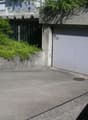 concrete building with a garage door, concrete barrier, small garden with green bush