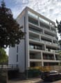 Multi-story apartment building with balconies, glass windows, and a modern, minimalist design.