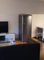 Living room with a sofa, glass table, white furniture, television, refrigerator, and a picture frame mounted on the wall.