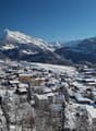 Mountain village in winter, snow covered houses, pine trees, and mountains in the background