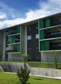 modern apartment building, green and gray exterior, multiple balconies, concrete fence, green lawn