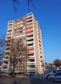 A tall residential building with multiple floors, balconies with orange shutters, and a beige and white exterior.