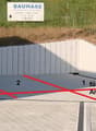 a sloped area with a concrete barrier for car and bicycle parking, a green grass field, and a white fence