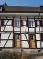 Two story house, white walls, brown trim, red shutters, two doors