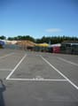 Paved parking lot with marked parking spaces, a large pile of wood debris, and various storage containers or dumpsters in the background.