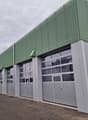 Warehouse, large garage doors, large windows, green and grey exterior, multiple entrances