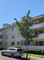 4 story apartment building, beige exterior, white balconies, street view, cars parked