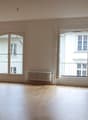 large empty room, wooden floor, three large windows with doors, radiators on the wall, white walls