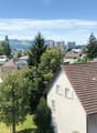 The image shows a residential neighborhood with a mix of single-family homes and multi-story apartment buildings. The area is surrounded by lush greenery, including trees and well-maintained lawns. The buildings have a mix of architectural styles, with so