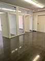The image shows an empty office space with a tiled floor and glass-paneled doors. The room has a clean, modern appearance with neutral-colored walls and overhead lighting.