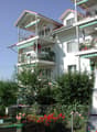 3 story white building, multiple balconies, green plants, shrubs