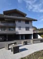3 story building, grey, underground garage, multiple balconies, mountain view, car in the driveway