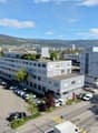 Multi-story office building with parking lot, surrounded by hills and mountains in the background