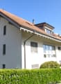 White house with red roof, multiple windows, hedges in front, chimneys