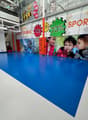 Large indoor retail space with blue flooring, various sports and outdoor equipment brands displayed on the walls, and signs advertising sales and discounts.