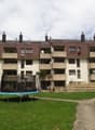 Apartment building with multiple floors, balconies, and a garden in front.