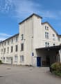3-story office building, beige exterior, multiple windows, blue door, parking lot in front, green vegetation, street light