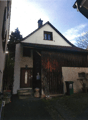 2 story house, white walls, brown roof, wooden door, steps leading to the entrance, trash bin, plants