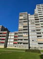 high rise apartment building, multiple floors, concrete exterior, red awnings, balconies, windows, greenery in front