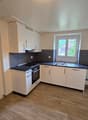 Spacious kitchen with white cabinets, black countertops, stainless steel appliances, and hardwood flooring. The kitchen has an L-shaped layout with a window providing natural light.